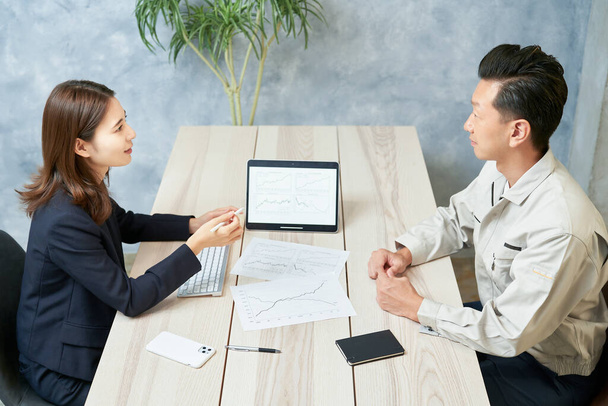 A woman in a suit meeting with a man in work clothes at office - Photo, Image