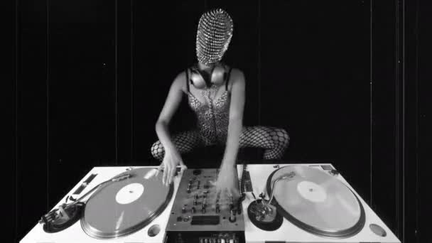 Masked female dj playing with turntables in sparkling silver costume with aged film in black and white - Imágenes, Vídeo