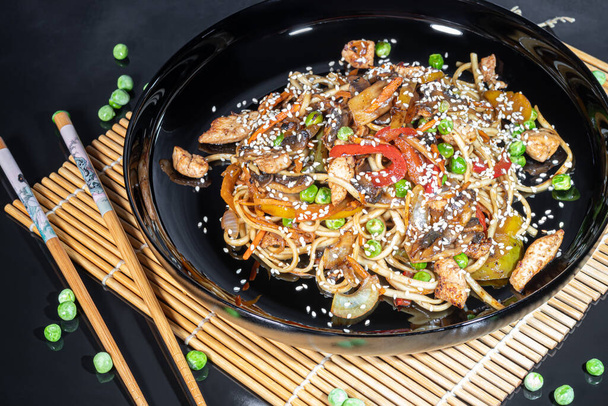 Udon noodles with meat, mushrooms and vegetables. Sprinkled with sesame seeds. Asian food, roast on black background, copy space - Foto, Imagen