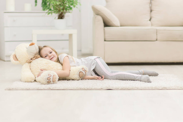 Photo of little girl laying on the floor with teddy bear. Concept of small blond girl. - Fotó, kép
