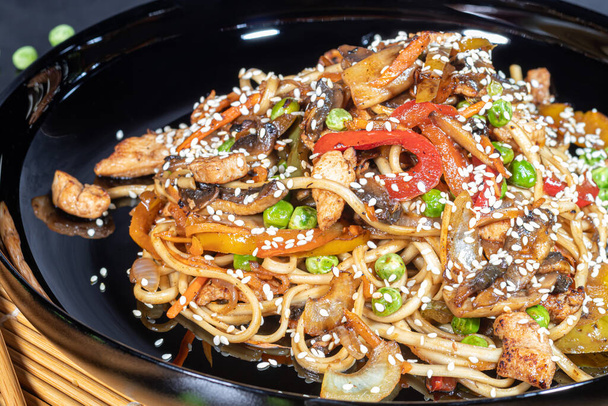 Udon noodles with meat, mushrooms and vegetables. Sprinkled with sesame seeds. Asian food, roast on black background, copy space - Foto, Imagem