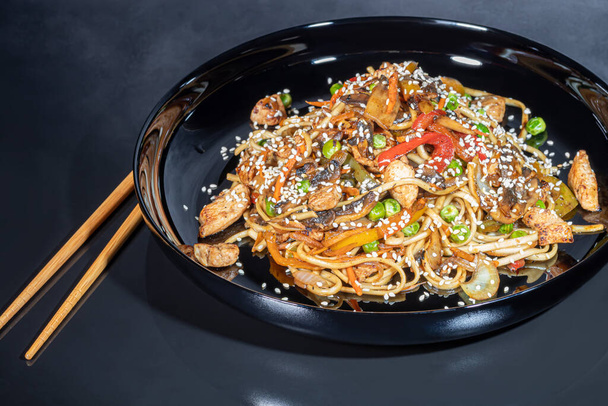 Udon noodles with meat, mushrooms and vegetables. Sprinkled with sesame seeds. Asian food, roast on black background, copy space - Foto, imagen