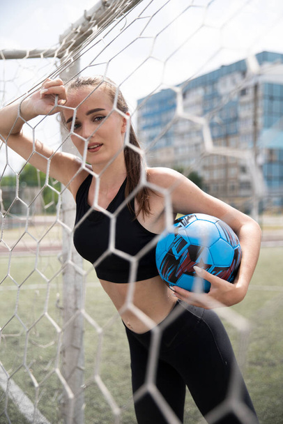 Μοντέλο με μπάλα ποδοσφαίρου στο τέρμα του ποδοσφαίρου. Σέξι αθλήτρια με μπάλα. - Φωτογραφία, εικόνα