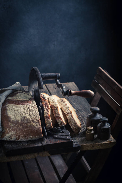 Healthy and tasty loaf of bread with on old slicer. A loaf of bread on a crumb slicer. - Foto, imagen
