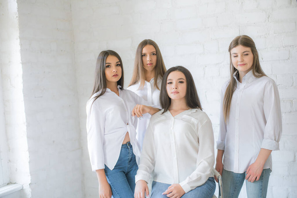 Pretty teenage girls models in trendy jeans and white shirts in the studio against the background of a white brick wall. Teenage fashion. beauty and fashion - Zdjęcie, obraz