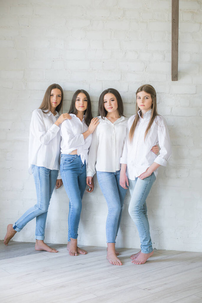 Красивые девушки-подростки модели в модных джинсах и белых рубашках в студии на фоне белой кирпичной стены. Подростковая мода. красота и мода - Фото, изображение