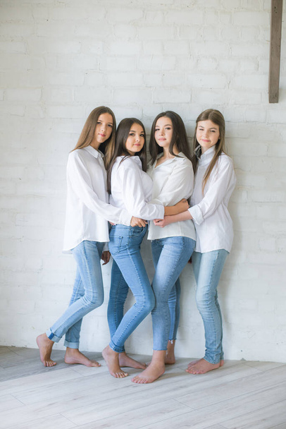 Красивые девушки-подростки модели в модных джинсах и белых рубашках в студии на фоне белой кирпичной стены. Подростковая мода. красота и мода - Фото, изображение