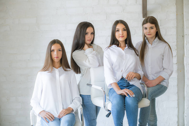 Pretty teenage girls models in trendy jeans and white shirts in the studio against the background of a white brick wall. Teenage fashion. beauty and fashion - Фото, изображение