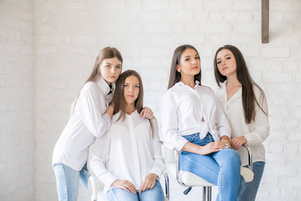 Pretty teenage girls models in trendy jeans and white shirts in the studio against the background of a white brick wall. Teenage fashion. beauty and fashion - Fotó, kép