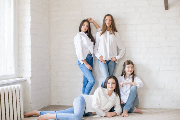 Pretty teenage girls models in trendy jeans and white shirts in the studio against the background of a white brick wall. Teenage fashion. beauty and fashion - Фото, изображение