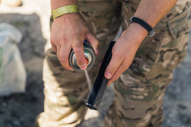 Close-up of gunsmith in camo clothing spraying barrel of gun. Gun maintenance. Repairing army equipment. Horizontal shot. High quality photo - Foto, Bild