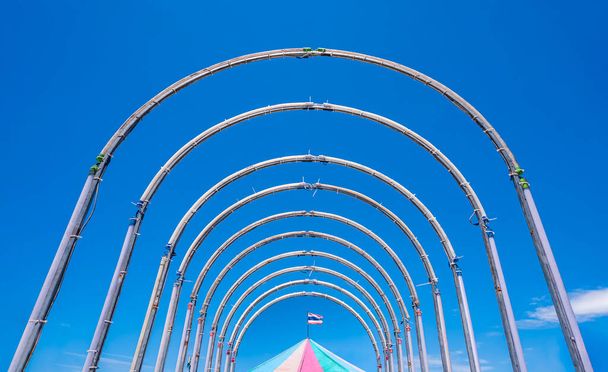 Симметрия и перспектива вид на стальной туннель игровой площадки структура оборудования и флуоресцентные лампы украшения с красочной палатки карусели на голубом ясном фоне неба - Фото, изображение