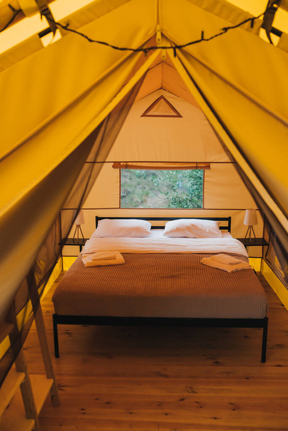 Interior of Cozy open glamping tent with light inside during dusk. Luxury camping tent for outdoor summer holiday and vacation. Lifestyle concept - Foto, imagen