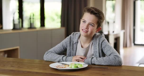 Unhappy child eating a healthy meal with vegetables at home and refusing to eat his greens. Little boy showing disgust and being fussy about dinner, lunch food. Picky eater making facial expression. - Video, Çekim