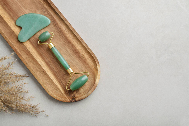 Facial jade massage rollers and gua sha massager made from natural jade stone on light concrete background, top view - Foto, Bild
