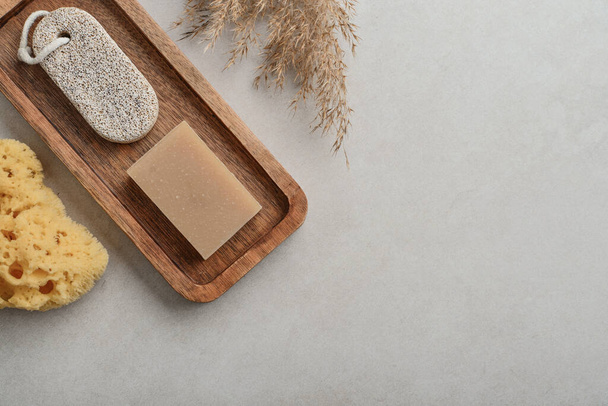 Natural soap bars and pumice stone on wooden tray with various toiletries on a light concrete background, top view - Photo, image