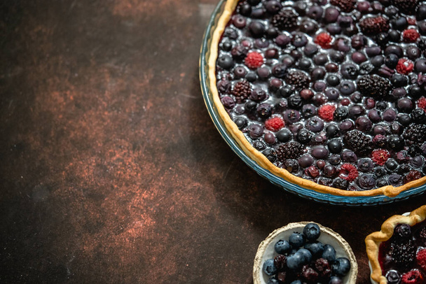 Homemade autumn sweet berry pie on dark rustic background. Served with fresh forest fruis. Top view, flat lay with copy space. - 写真・画像