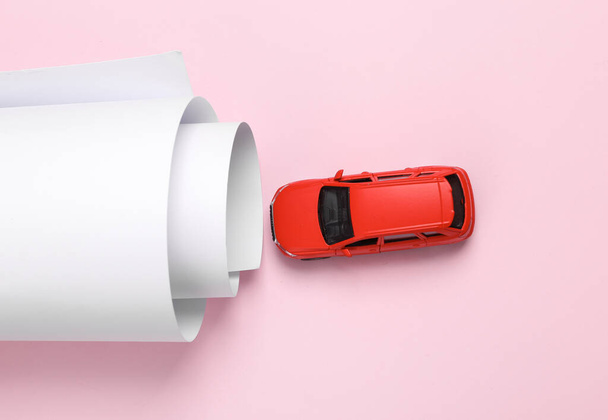Minimalistyczna martwa natura. Zabawkowy samochód z papierowym tunelem na różowym tle. Układy płaskie - Zdjęcie, obraz