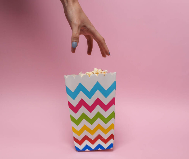 Жінка голодна рука тягнеться до попкорн коробки на рожевому фоні
 - Фото, зображення