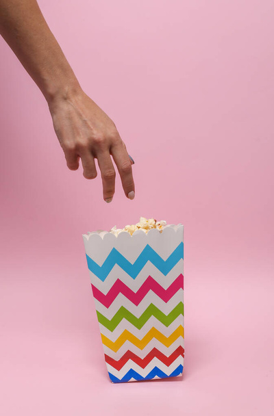 Woman's hungry hand reaching for popcorn box on pink background - Fotó, kép