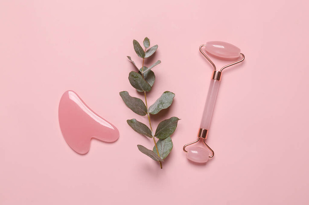 Massage facial roller and a stone with a sprig of eucalyptus on a pink background. Beauty, facial skin care concept - Foto, afbeelding