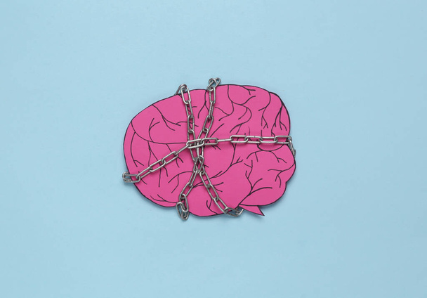 Paper brain wrapped with a steel chain on a blue background. Lack of ideas or headache - 写真・画像