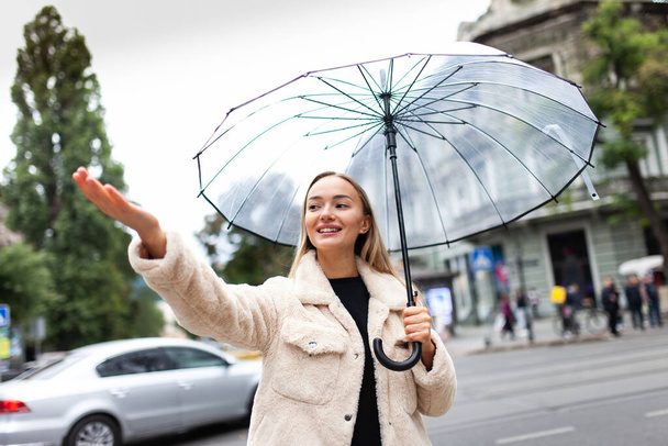 fashion blonde woman with a transparent umbrella checks the rain in the city. Lifestyle, rainy weather - Foto, Imagen