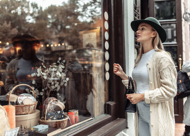 Pretty young woman in fashion clothes looks in the shop window. Shopping concept - Photo, image