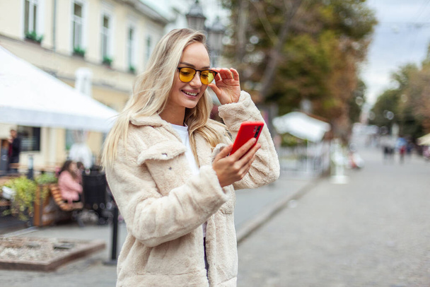 cute stylish woman in yellow sunglasses using smartphone in the city - Photo, Image