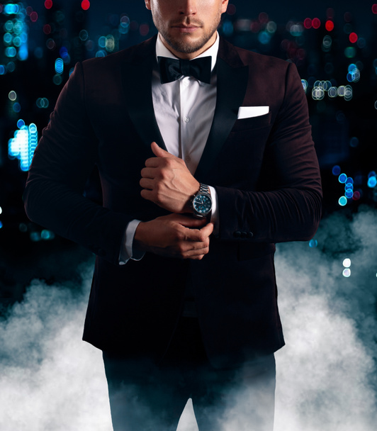 Secret agent in bow tie adjusting watch in city night - Photo, Image