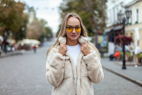 Portrait of a stylish fashion woman in yellow sunglasses and a fur coat in the city. Lifestyle - Photo, image