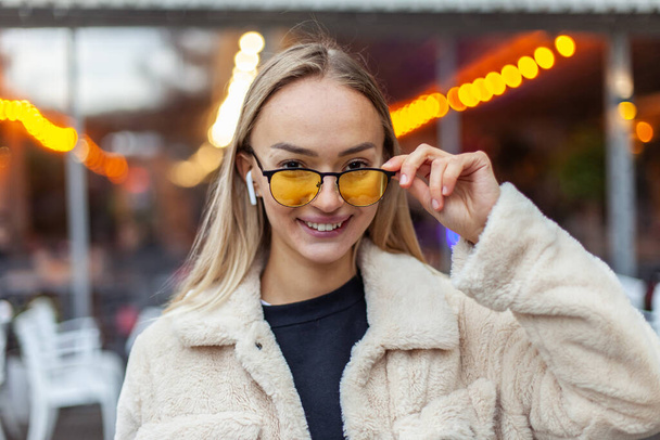 Портрет усміхненої молодої блондинки в жовтих сонцезахисних окулярах у вечірньому місті
 - Фото, зображення