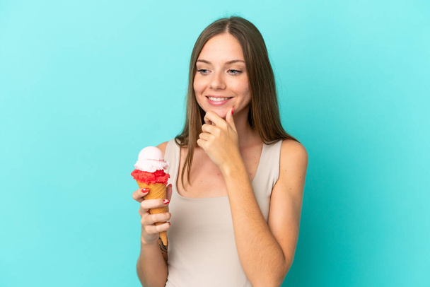 Nuori liettualainen nainen, jolla on sinisellä pohjalla eristetty cornet-jäätelö, katsoo sivulle ja hymyilee - Valokuva, kuva
