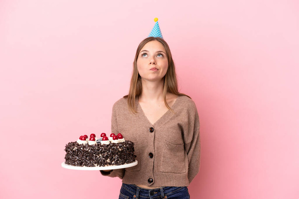 Young Lithuanian woman holding birthday cake isolated on pink background and looking up - Foto, Imagem
