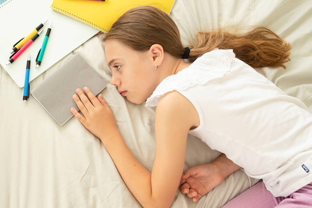 Child does homework, prepares for tests, 10-year-old unhappy girl is tired, resting near notebooks lying in the bedroom. Concept of home school, dyslexia, discipline in study, educational problems. - Photo, Image