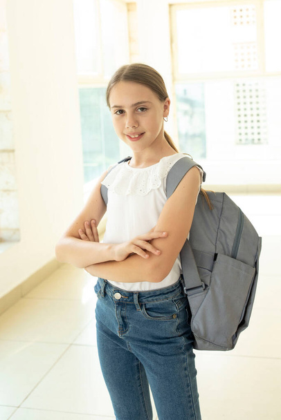 One schoolgirl with a backpack standing in school hall with large windows. Happy 10 years old girl, caucasian. Eye contact. Back to school, education, learning concept. Indoor. - Foto, Imagem