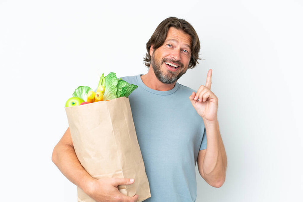 Senior holandês homem segurando supermercado saco de compras sobre fundo isolado pensando uma ideia apontando o dedo para cima - Foto, Imagem