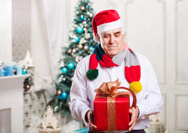 älterer Mann mit roter Geschenkschachtel auf weihnachtlichem Hintergrund - Foto, Bild