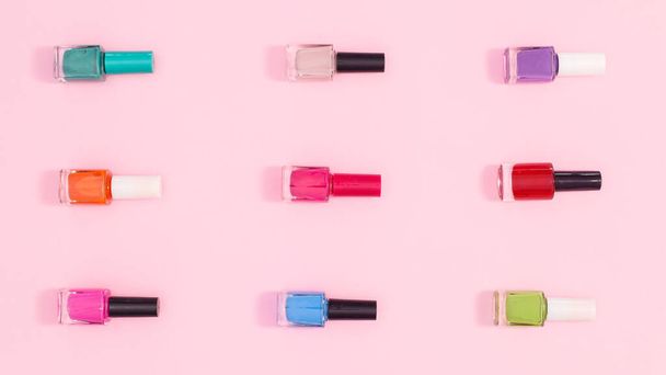 Nail polish bottles in various colors  make patern on pastel pink background. Flat lay - Fotó, kép