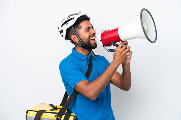 Young Brazilian man with thermal backpack isolated on white background shouting through a megaphone - Photo, Image