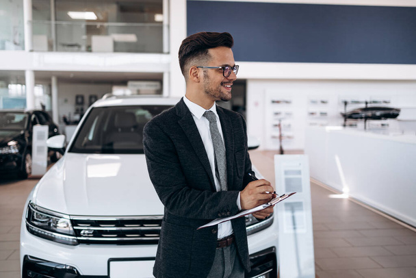 Good looking, cheerful and friendly salesman poses in a car salon or showroom. - Foto, Bild