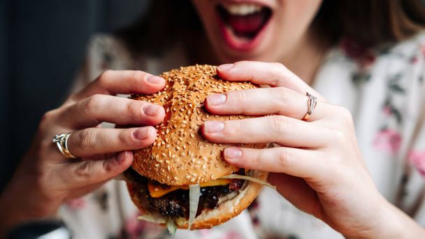 Woman hamburger eat. Hungry Caucasian Female Eating Tasty Burger. Fast food, people and unhealthy eating concept - Foto, Imagen