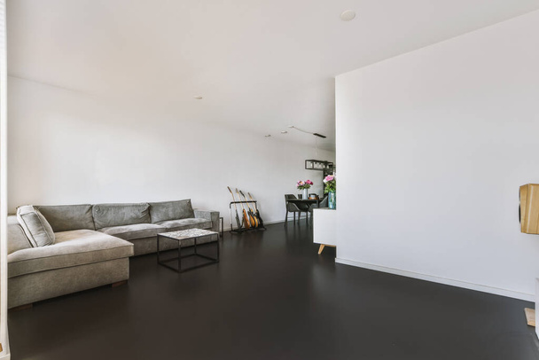 Nowoczesny minimalistyczny styl wnętrza jasny apartament typu studio z drewnianym stołem i krzesłami w strefie jadalnej między otwartą kuchnią i salonem z białymi ścianami i parkietem - Zdjęcie, obraz