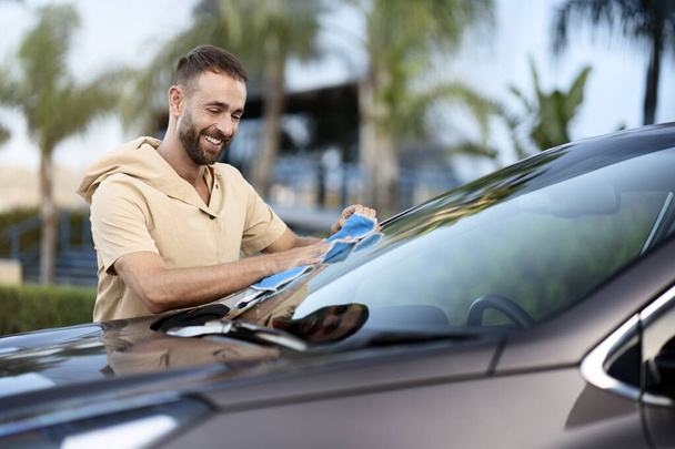 Portrait of smiling latin man cleaning car using micro fiber cloth. Car washing service concept - Foto, imagen