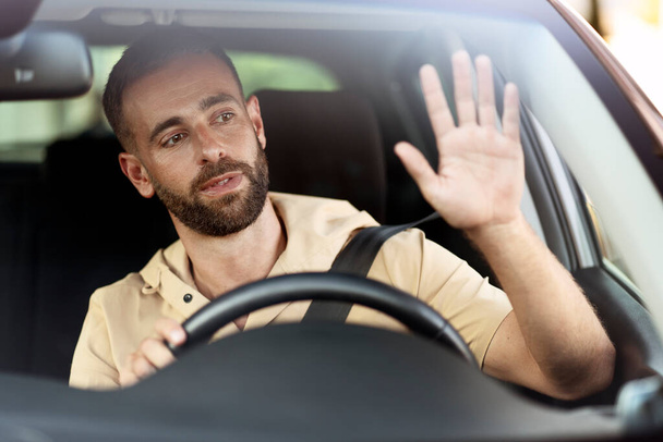 Un tassista barbuto pensieroso che saluta la mano seduto in macchina. Concetto di trasporto - Foto, immagini