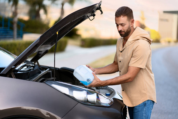 Latijnse man die ruitensproeiervloeistof giet om auto te reinigen. Autoserviceconcept - Foto, afbeelding