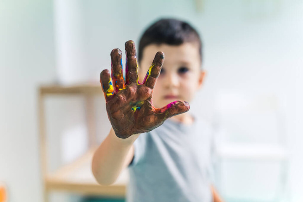 Toddler boy showing his colorful palm painted with washable and non-toxic paints after an art game at the nursery school. Finger painting for kids sensory skills, creativity and imagination - Foto, afbeelding