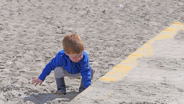Ragazzo dalla testa rossa che gioca con Bucket spade e Digger su una spiaggia di sabbia  - Foto, immagini