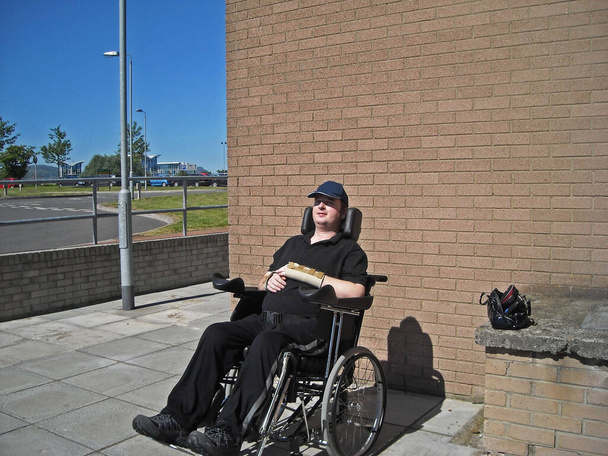 Mozgáskorlátozott kerekesszék-használó ül a napon a falnál - Fotó, kép