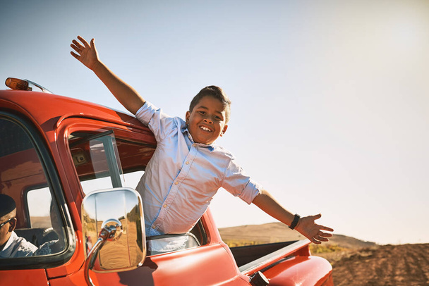 Take on life with open arms. a young cheerful boy leaning out of a red pickup truck with his arms stretched out while looking into the camera - Foto, Bild